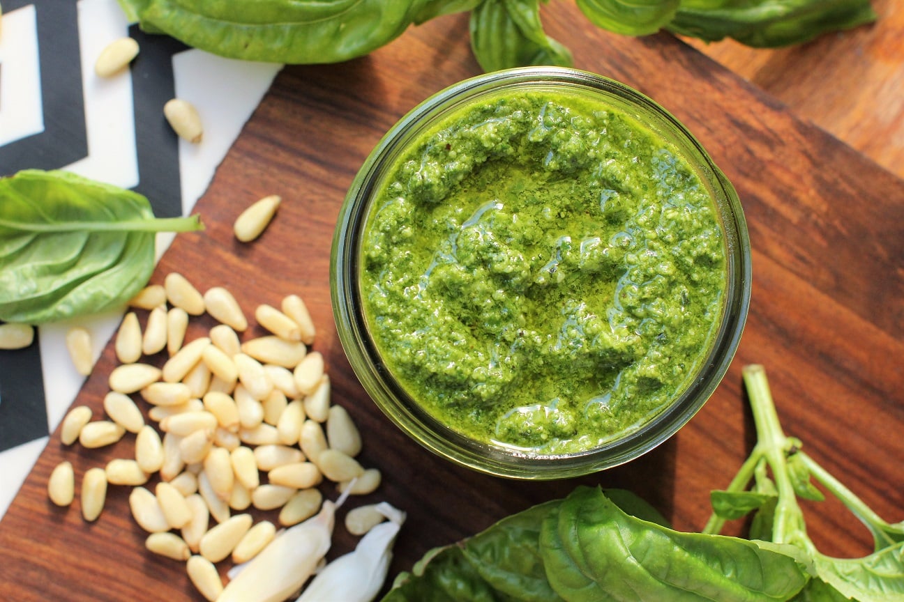 classic basil pesto, with pine nuts and garlic, looking down into the jar, with a pile of pine nuts beside it.