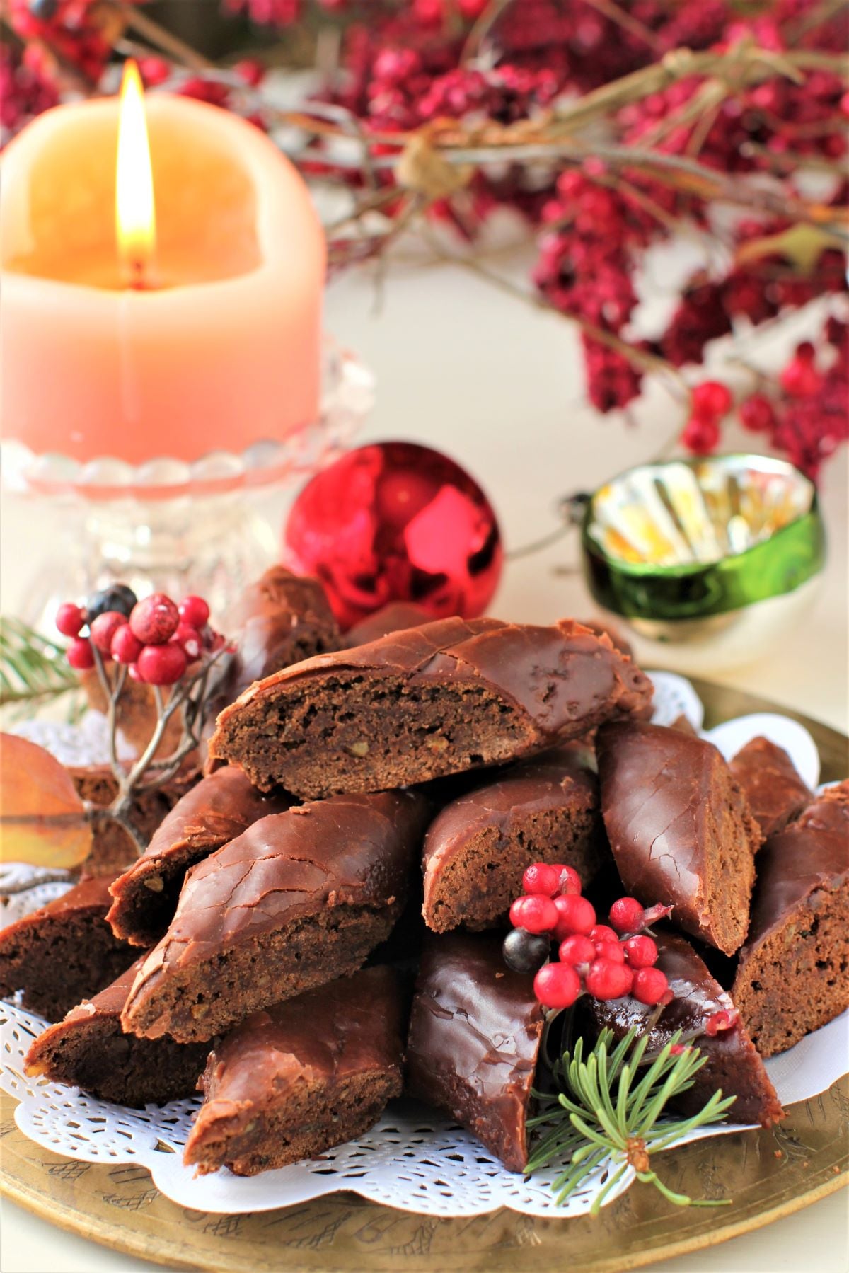 plate of German Magenbrot glowing in front of a lit candle and red berries in the background.