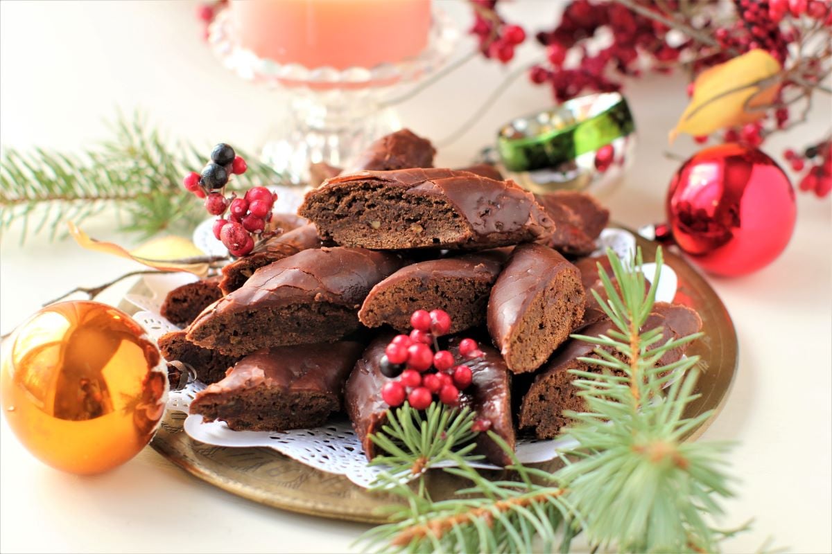 a plate of cut Magenbrot with Christmas berries and evergreen sprigs around it.