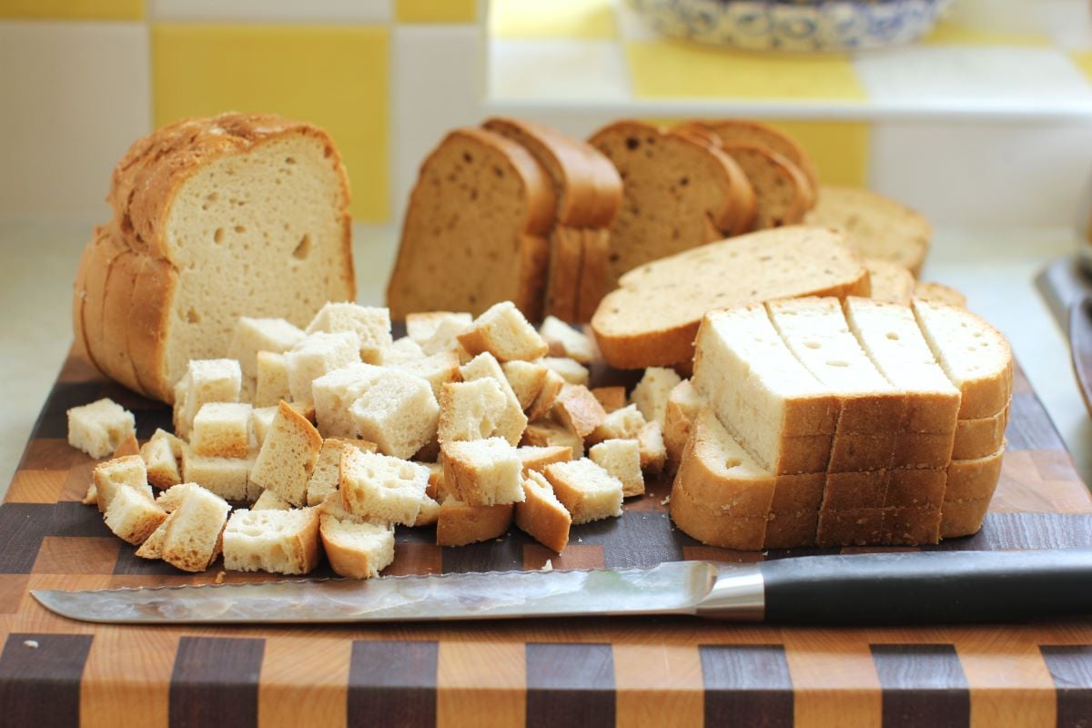 cutting board with stacks of bread slices and cubes being cut.