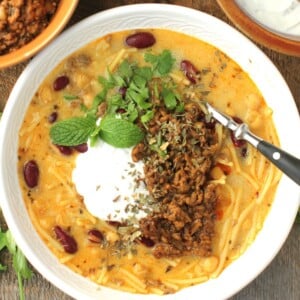 Aush soup thumbnail, top-down view of bowl of aush, topped with yogurt sauce and meat.