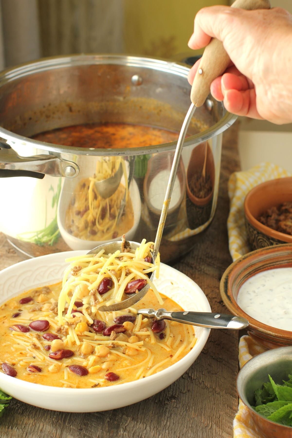 hand ladling aush noodles and beans into the bowl.