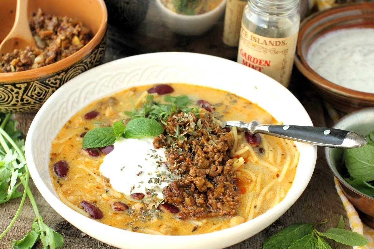 close-up of bowl of Aush Noodle Soup with jar of dried mint behind.