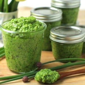 Thumbnail photo of a jar of chive pesto with spoonful in front, on a wooden cutting board.