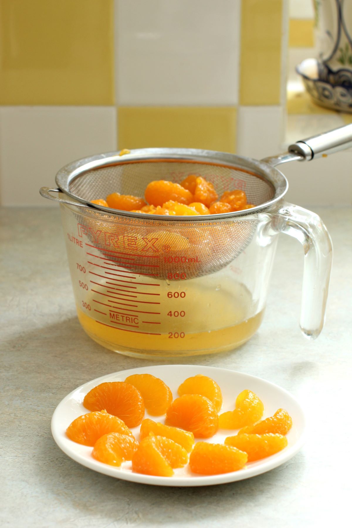 orange sections in a sieve set over a measuring cup. Small plate of orange segments in front.