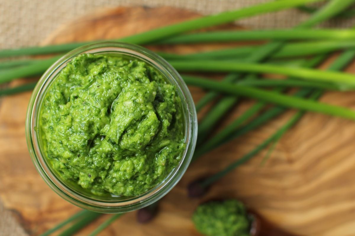 Top-down view of a jar of pest from the top, on a cutting board with chive stems.