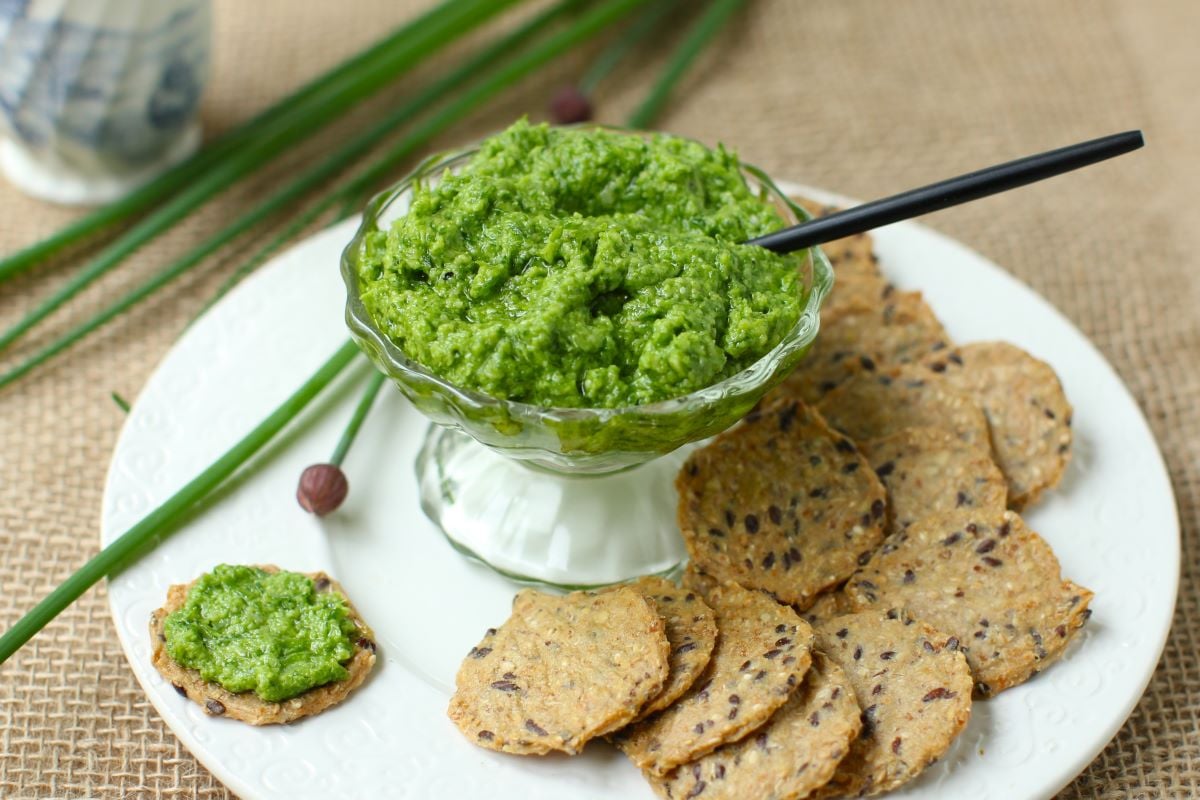A bowl of chive pesto with crackers on a white plate.