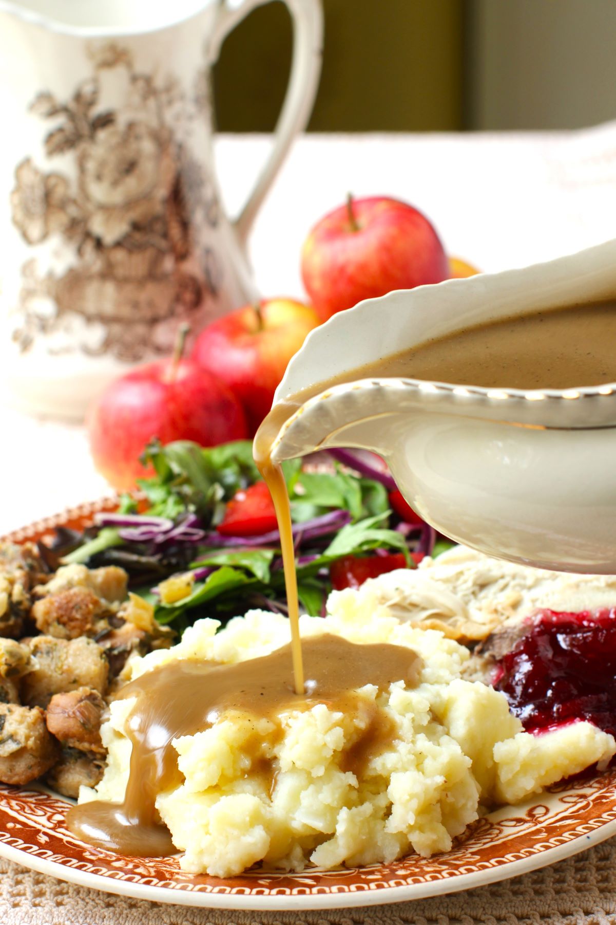 Pouring apple cider gravy onto a pile of mashed potatoes on a fully loaded plate of turkey dinner.