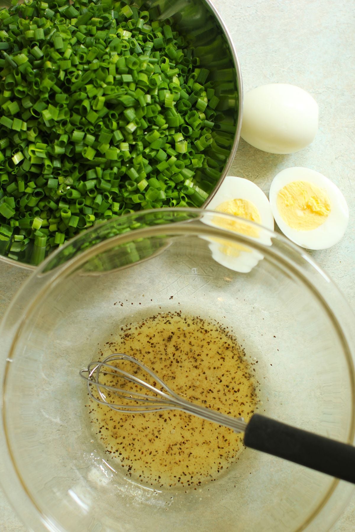 Chopped chives in a bowl, 2 hard-boiled eggs beside. Dressing whisked up in a bowl beside.
