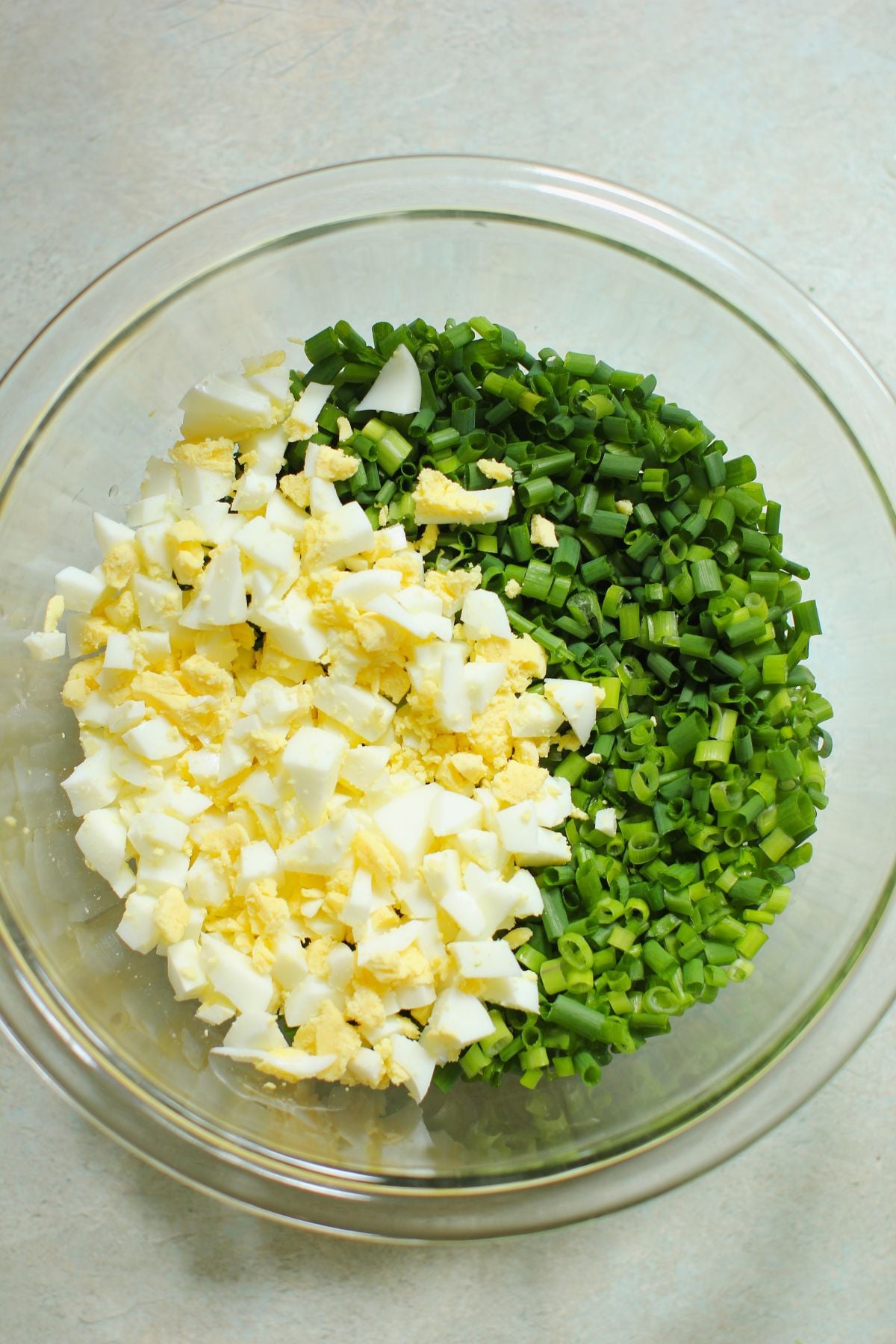 Chopped chives and eggs in a clear bowl.