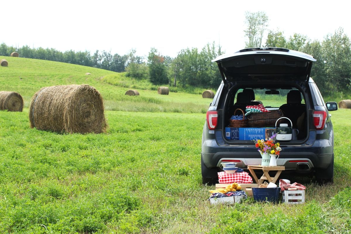 The back of the vehicle is open with picnic stuff inside it and on the ground behind it.