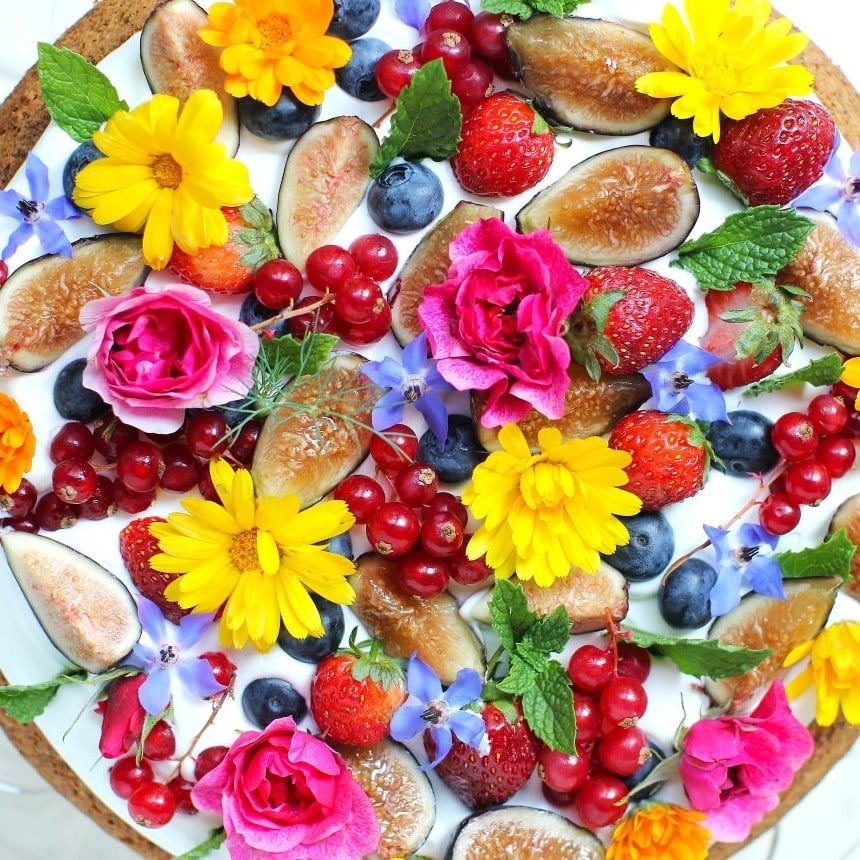 Top view of Fruit & Flower Almond Cake with figs, blueberries, strawberries, red curants, roses, calendulas, borage flowers, and mint leaves;