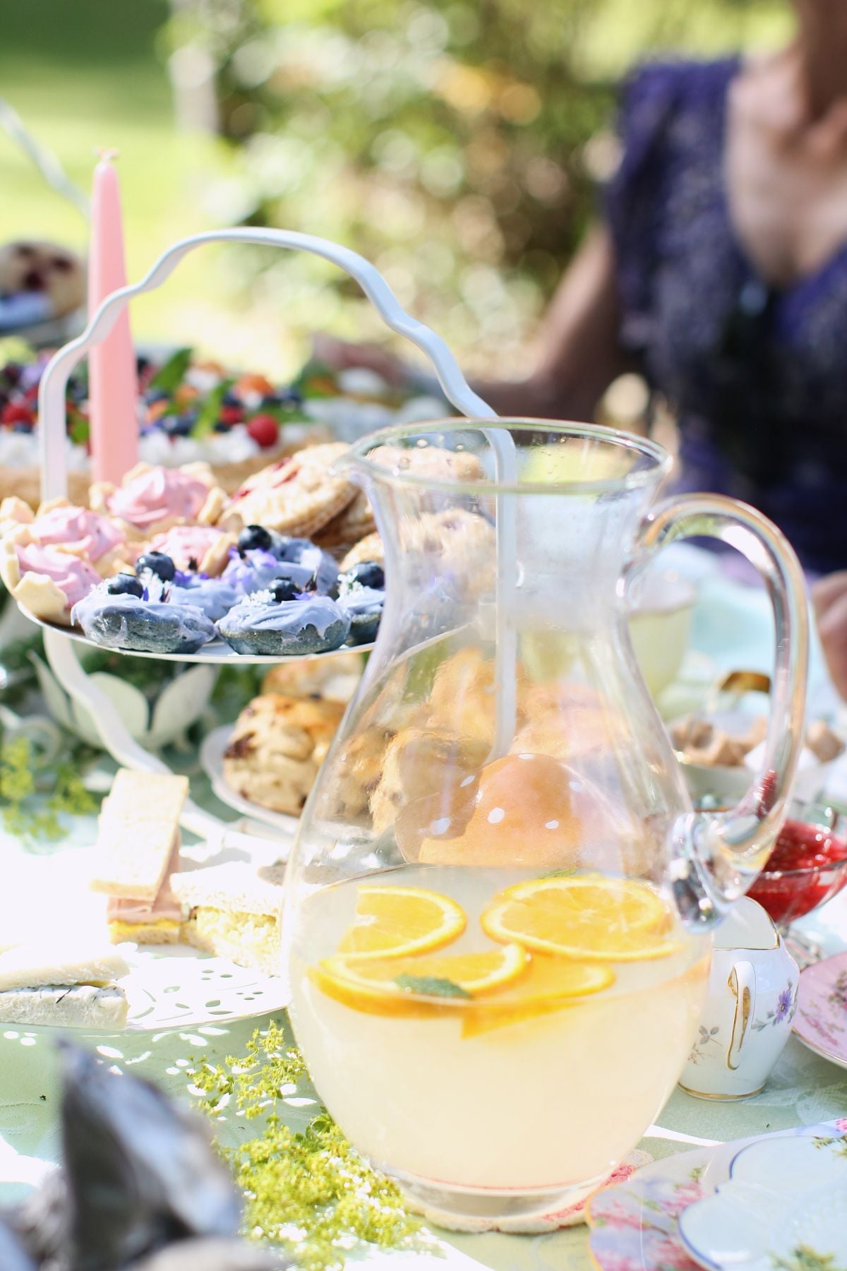 Tea table with goodies. Mini blue donuts on the 3-tiered cake stand. Pitcher of lemonade in front.
