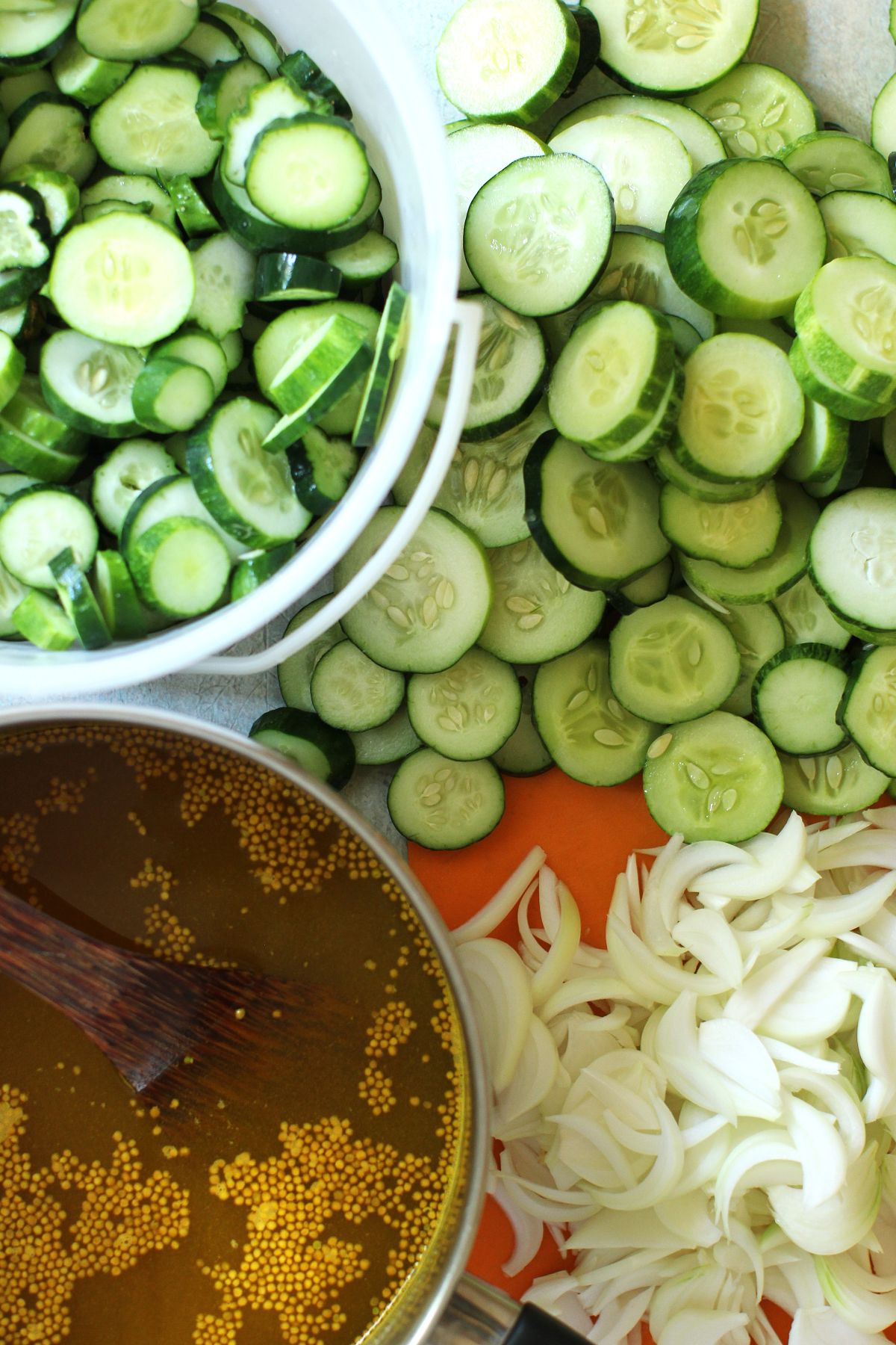 Piles of sliced cucumbers and onions and the cooked brine in a saucepan.
