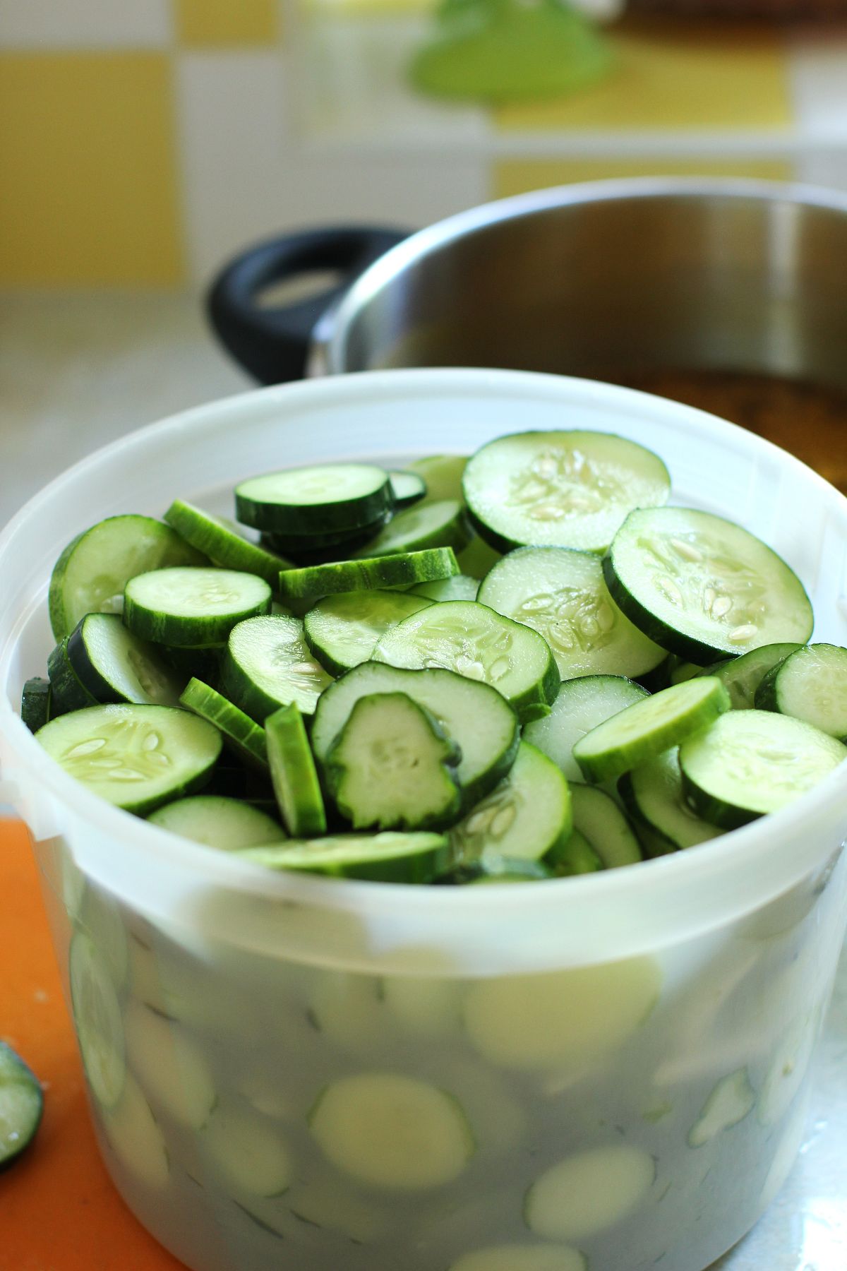 A plastic ice cream pail of sliced cucumbers.