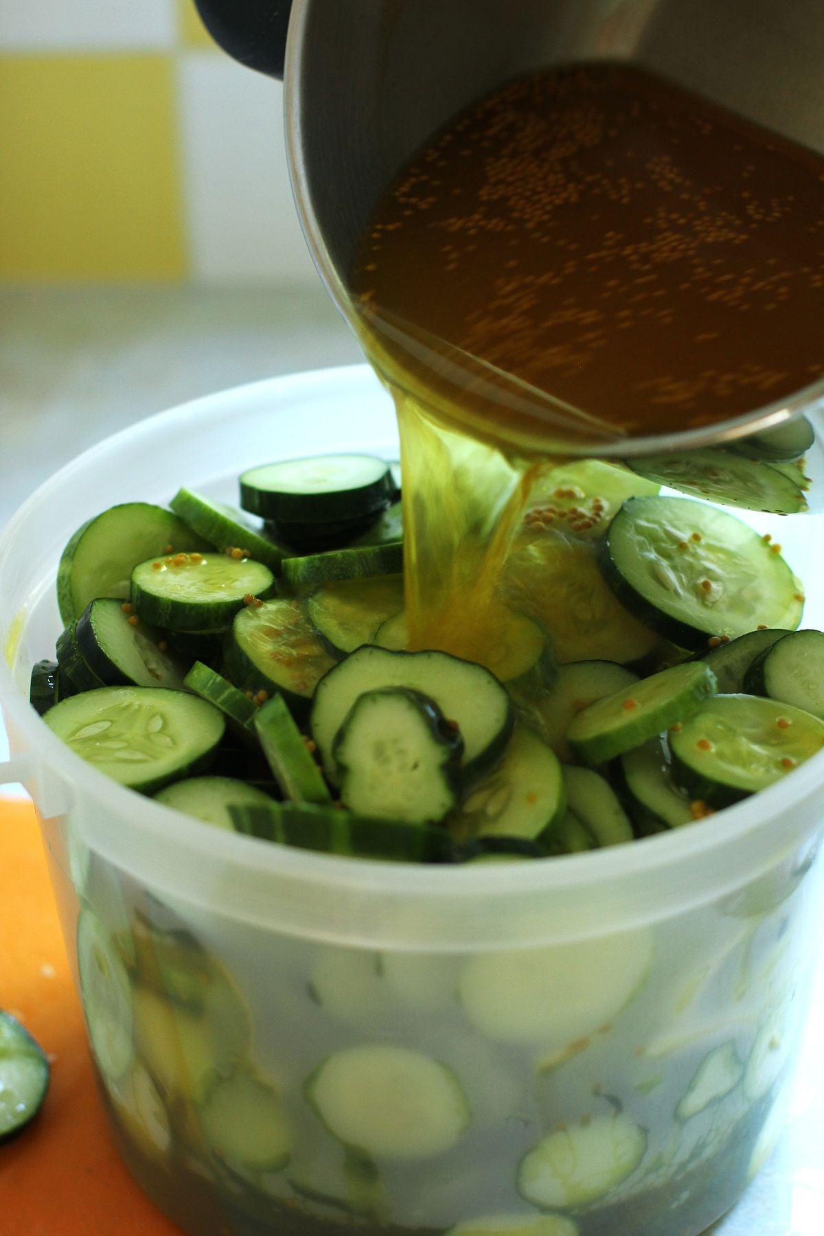Pouring the brine over the sliced cucumbers in the pail.