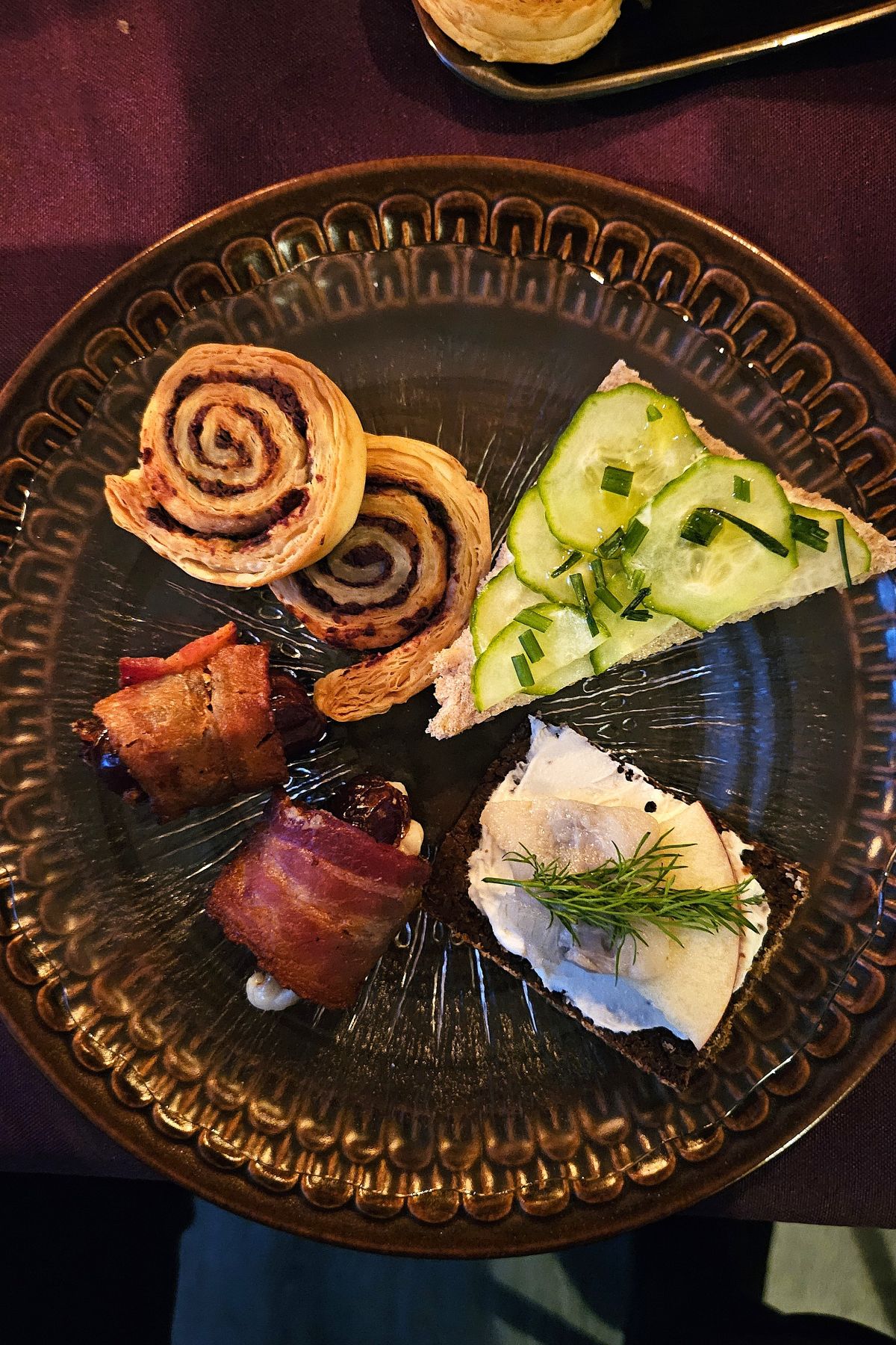 brown small plate of savouries, bacon wrapped dates, olive and anchovy spirals, cucumber sandwich, herring sandwich.