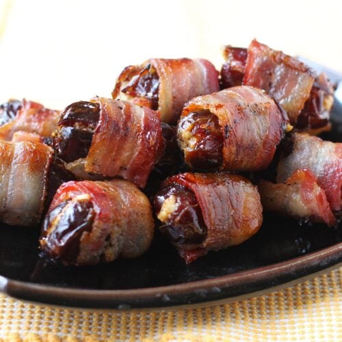 Bacon wrapped dates piled on a black platter, thumbnail photo.