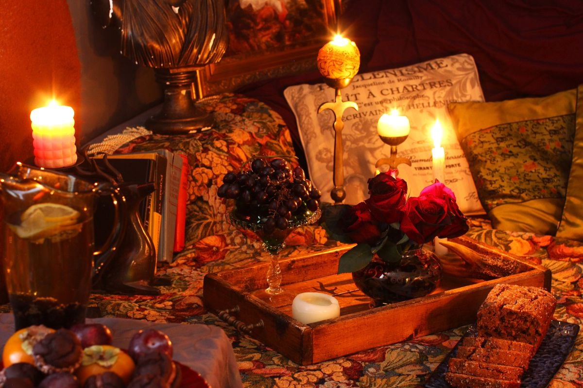 Candles, cushions, roses all set on a wooden tray on a tapestry covered couch.