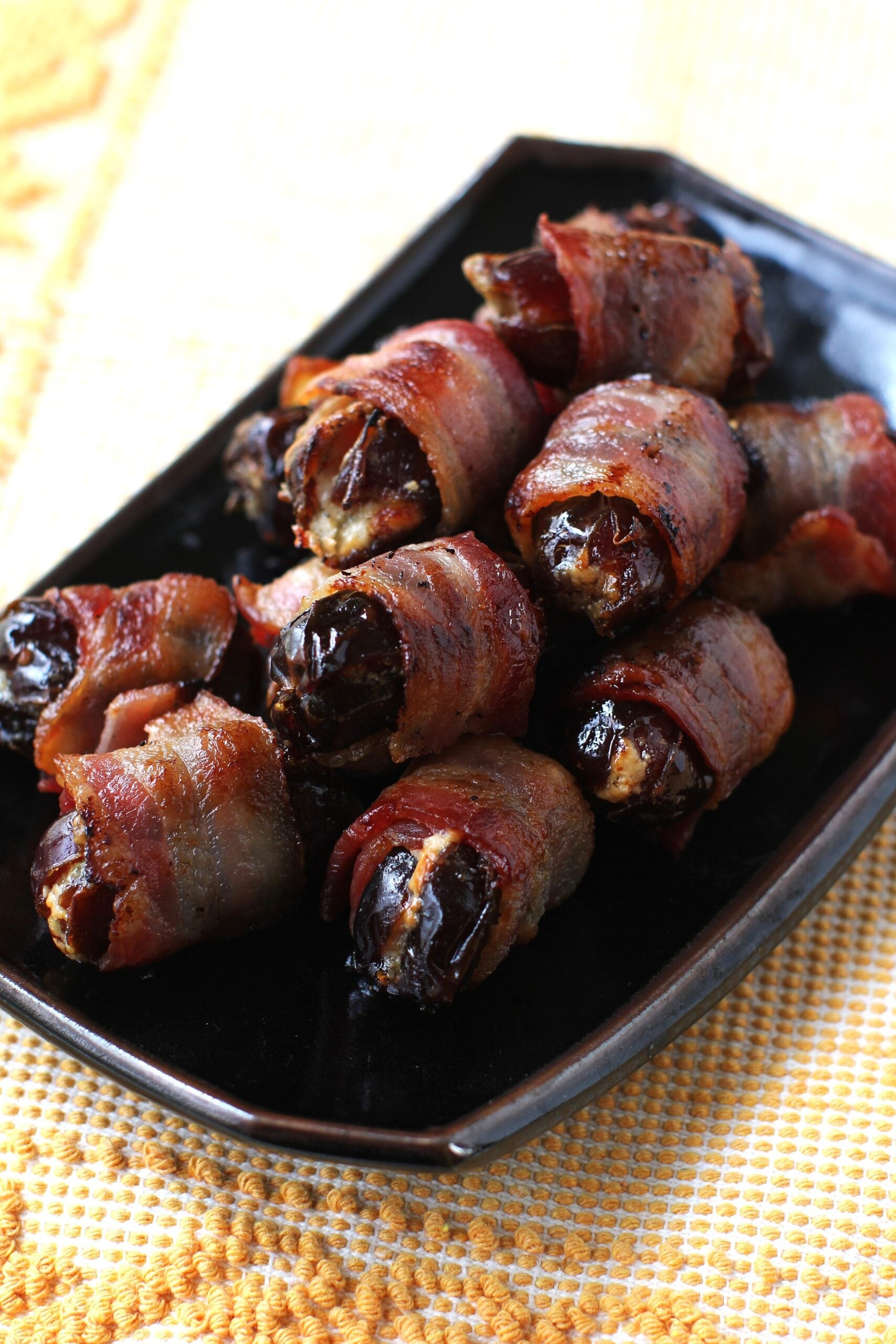 bacon wrapped dates on a rectangular black platter.
