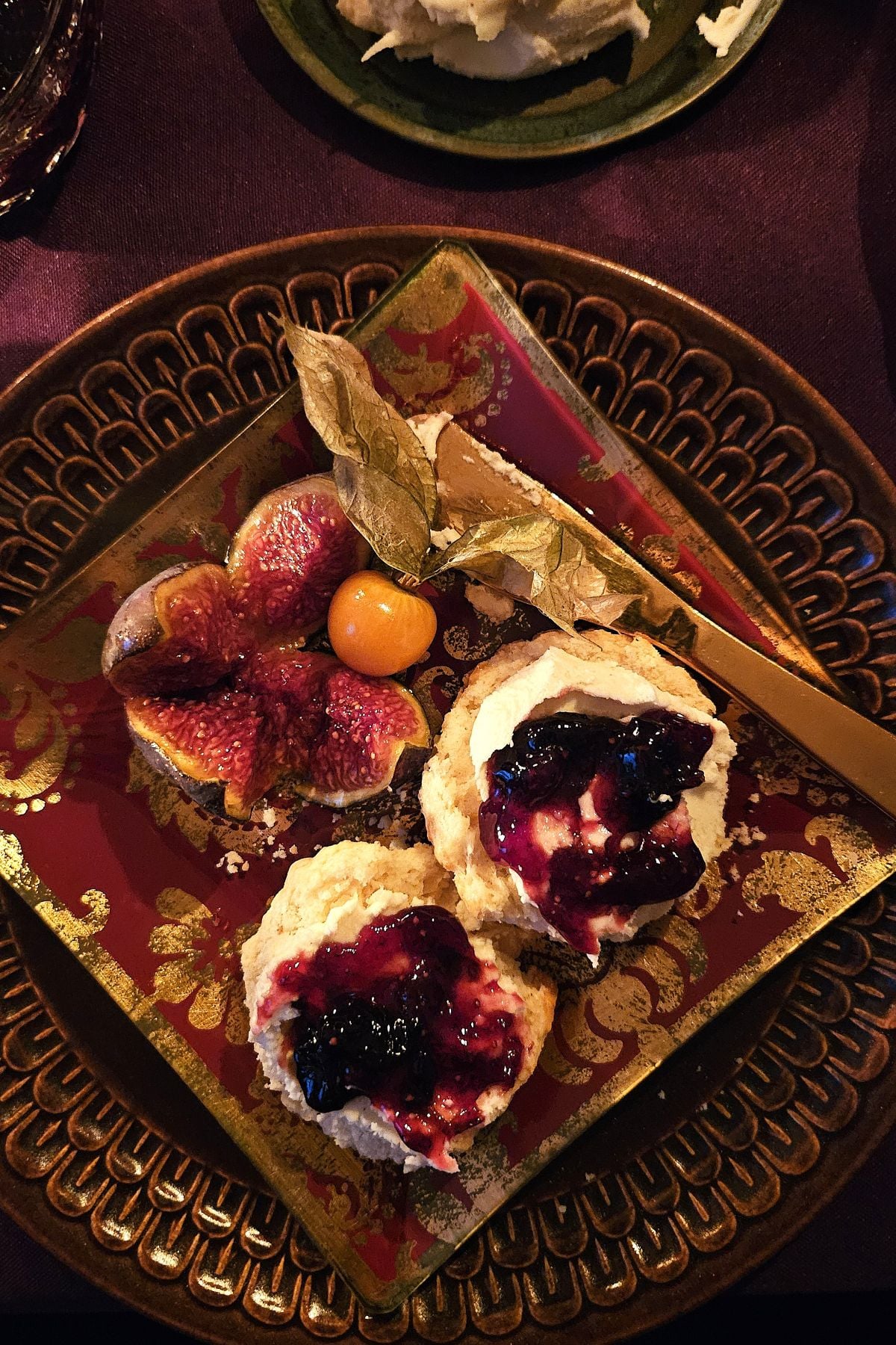 brown plate with scones spread with clotted cream and jam, fig, cape gooseberry.