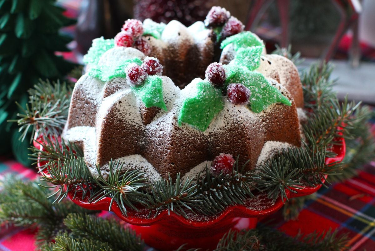 Horizontal photo of Gingerbread Bundt Cake on red plate, with spruce sprigs around it.