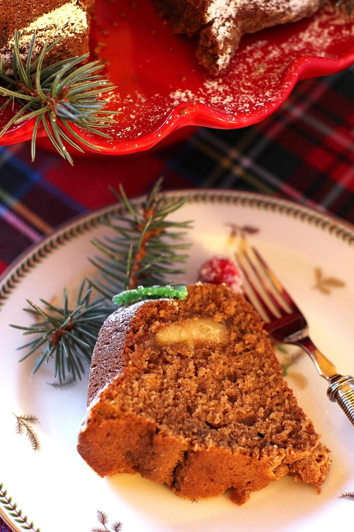 A slice of gingerbread bundt cake on a plate with a sprig of spruce.