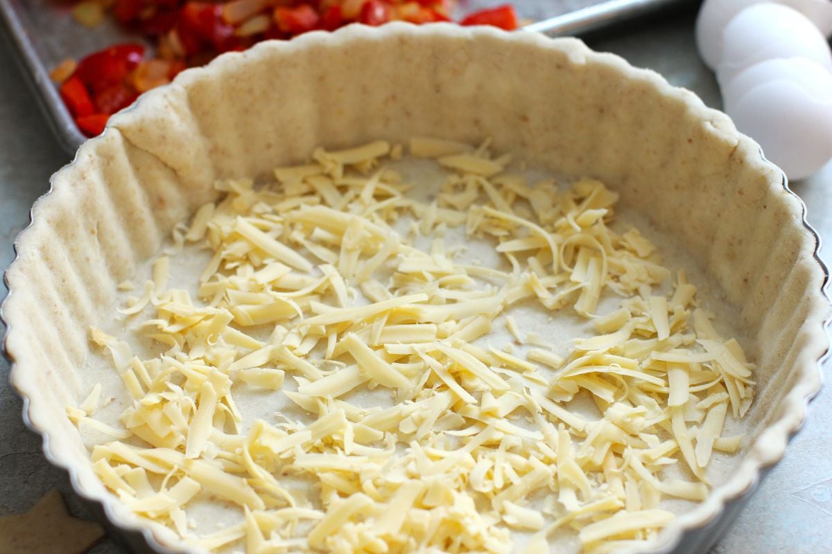Pastry crust in a fluted tart pan, filled with a thin layer of shredded gouda cheese.