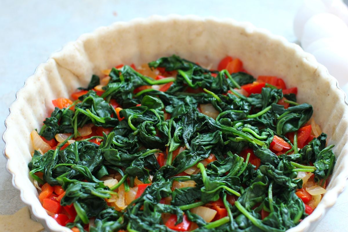 A layer of bright green cooked spinach spread over the sauteed peppers in the quiche crust.