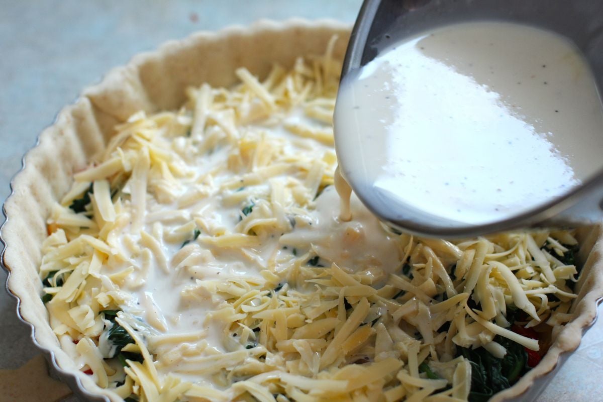 Pouring the beaten eggs onto the shredded cheese and filling in the crust.