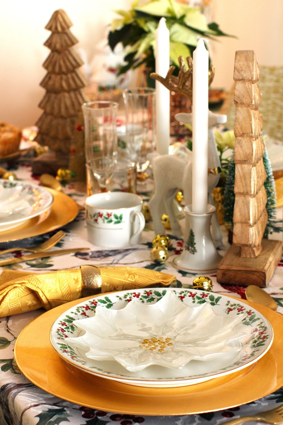 The table setting with a holly plate on gold charger, and white candles in china holders.
