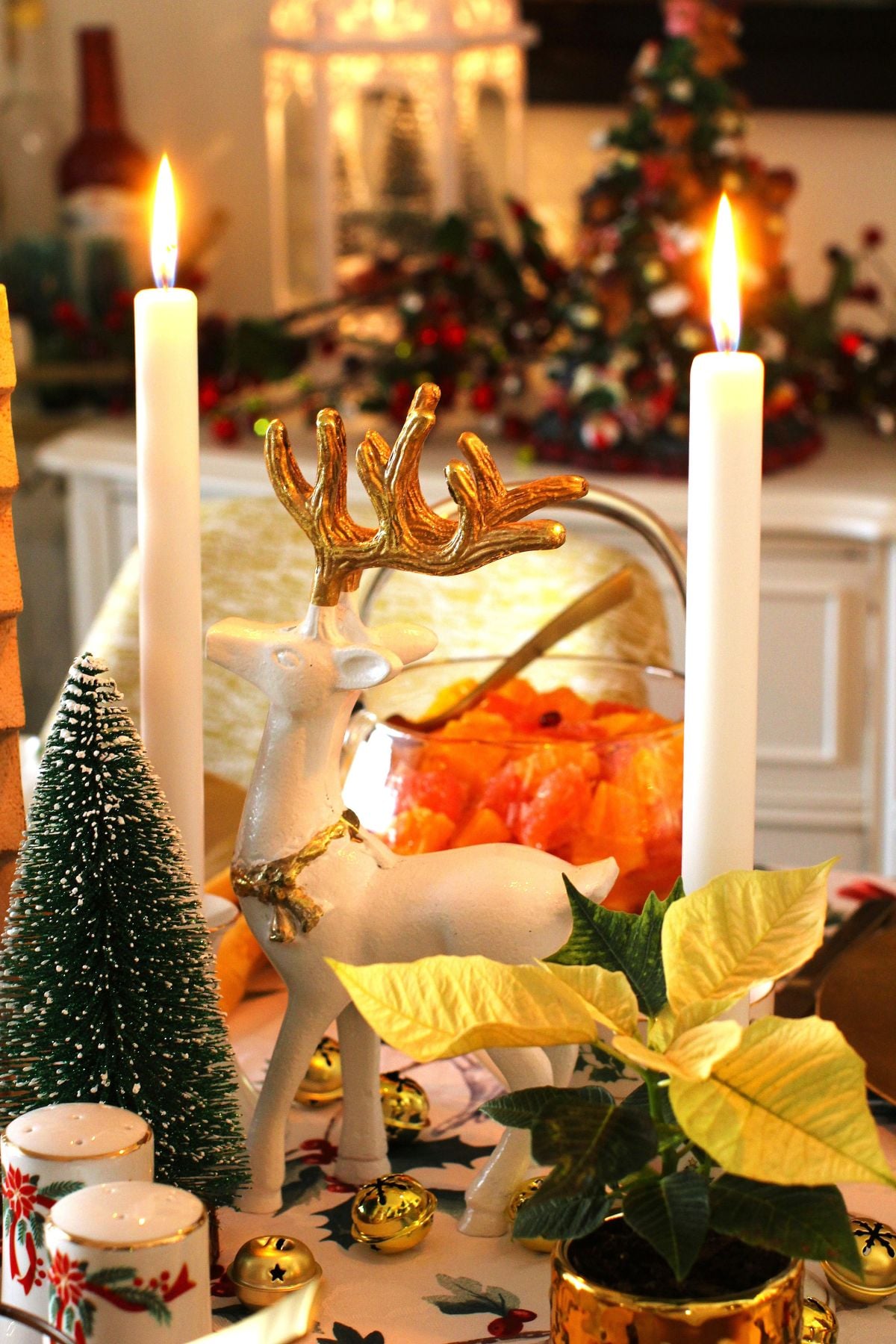 Two white candles and a white and gold reindeer in the middle on the Christmas table.