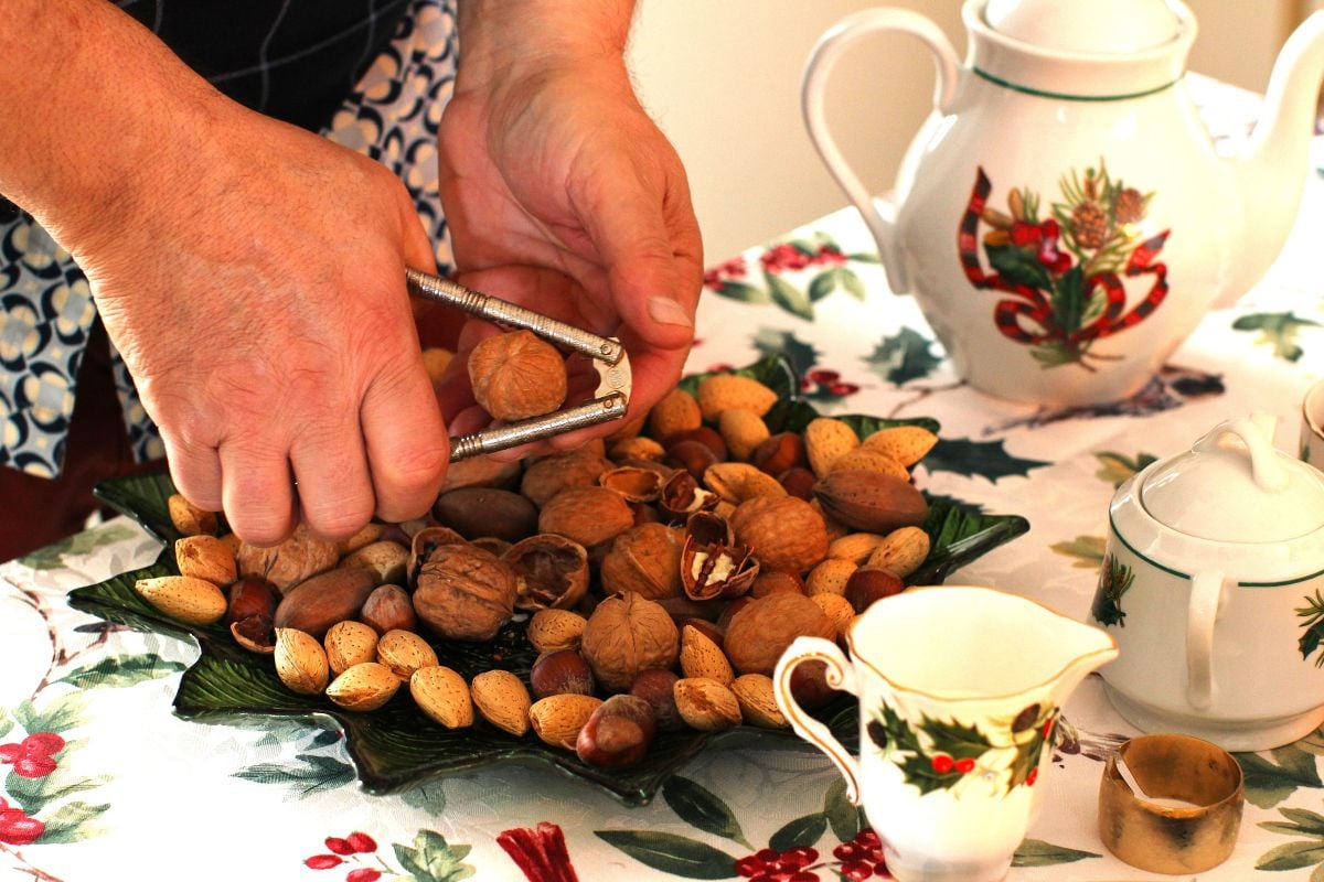 Two hands cracking a walnut over a bowl of whole assorted nuts.