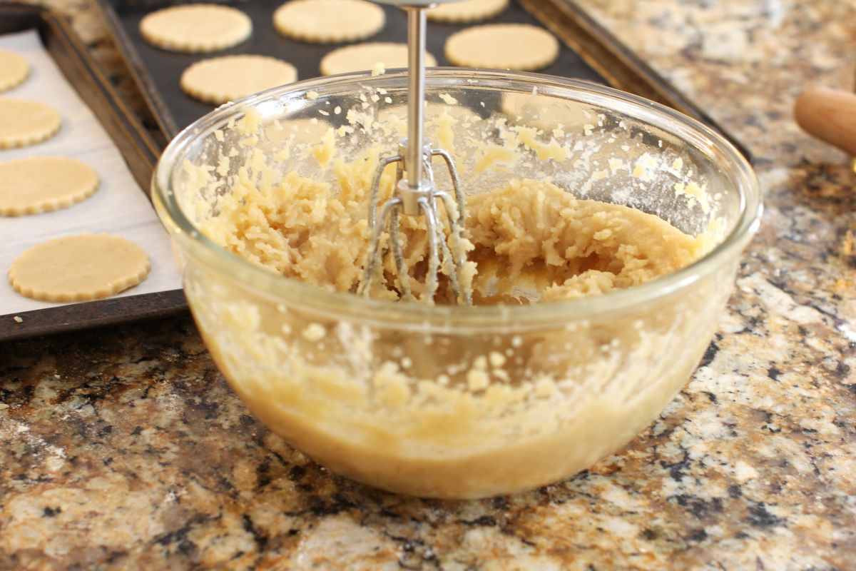 Clear glass bowl of almond paste dough with beaters in it.