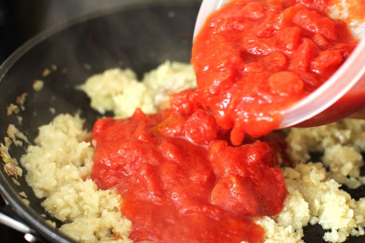 Pouring canned tomatoes onto the fried onions for sauce for the koshari.