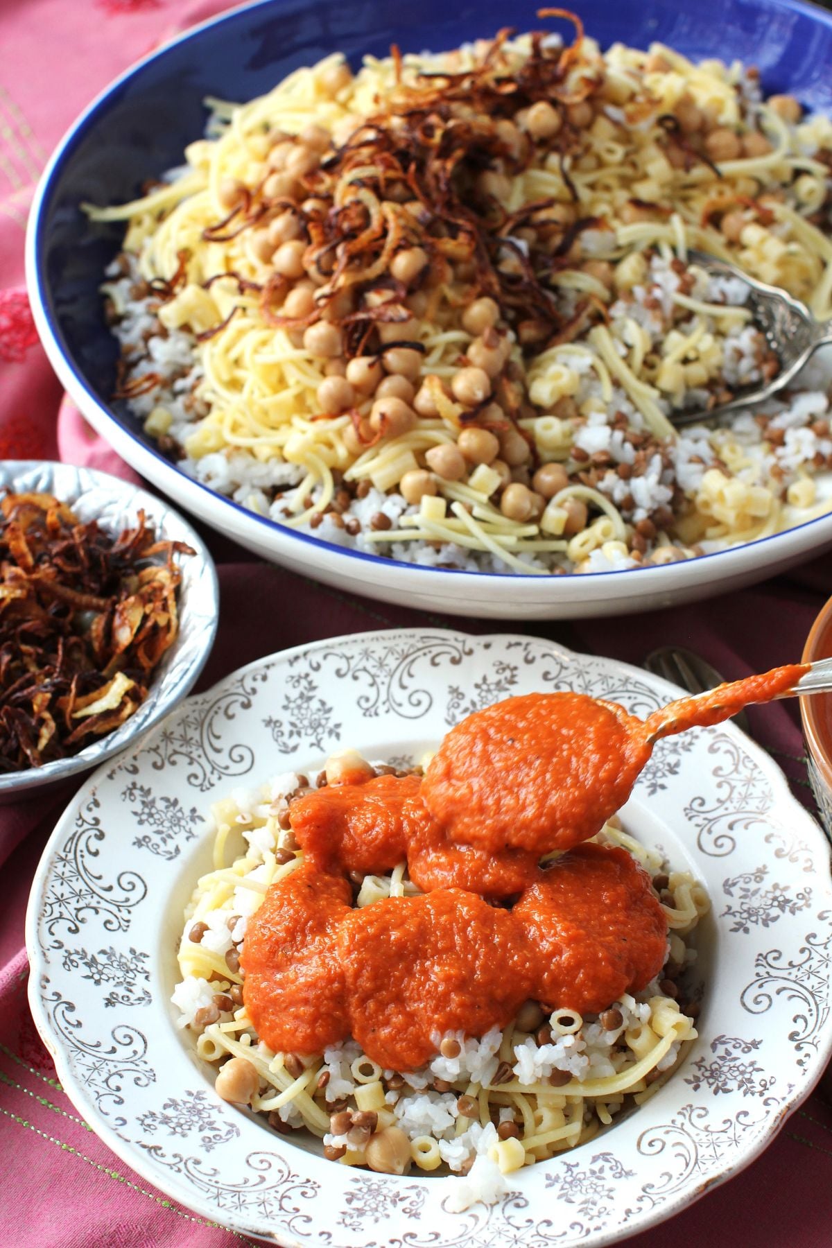 Spooning the tomato sauce onto the koshari in a rimmed soup plate.