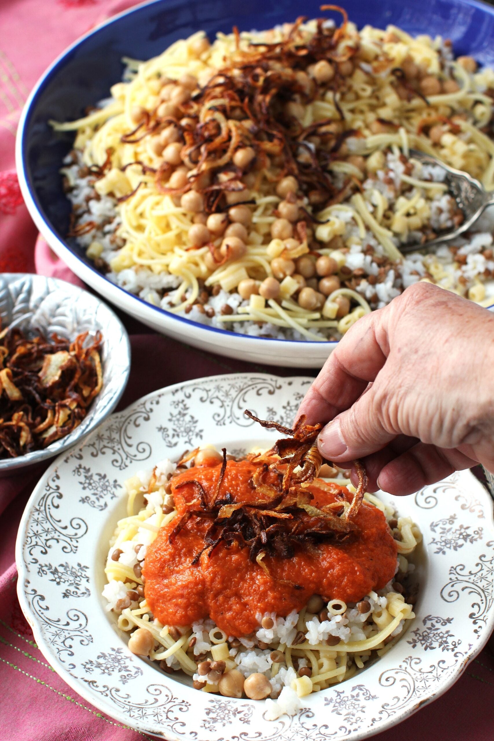 Adding a handful of crispy fried onions to the plate of koshari.