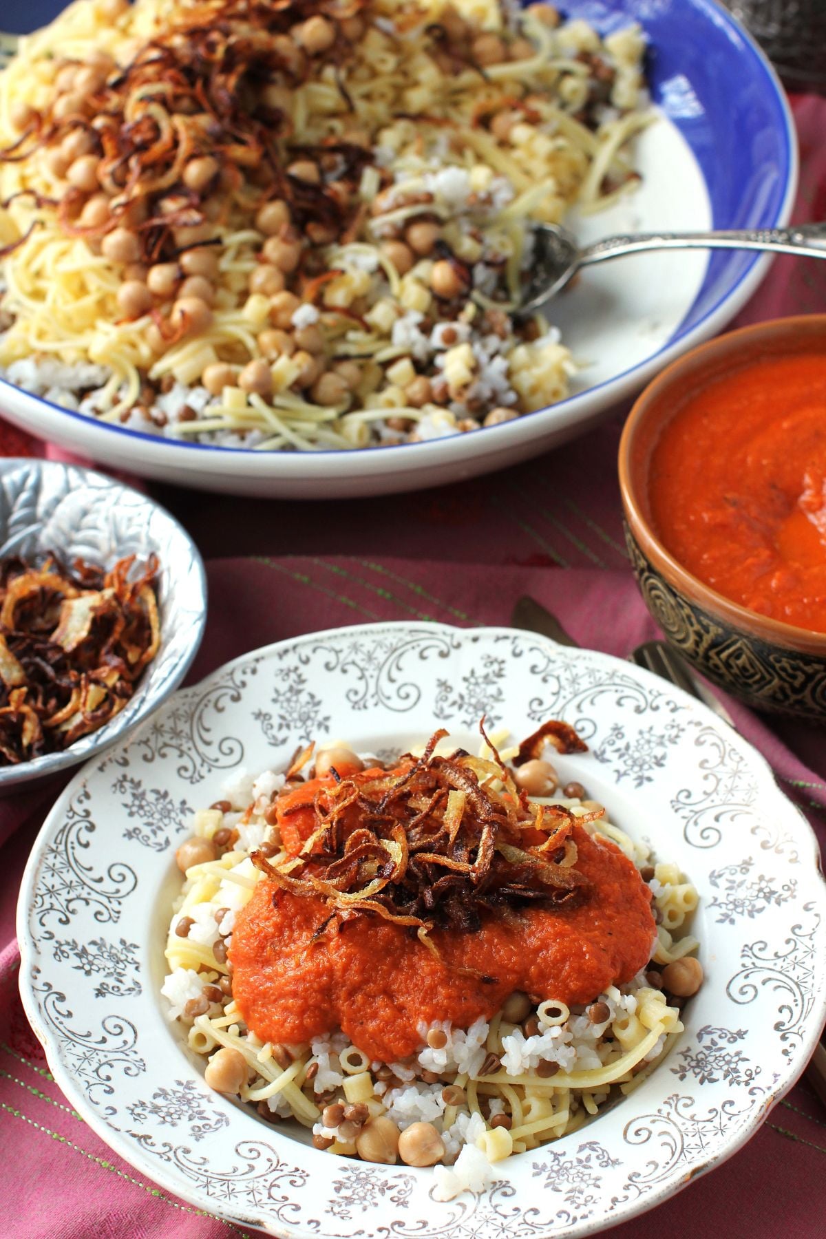 A plateful of koshari ready to eat, with large serving bowl behind.