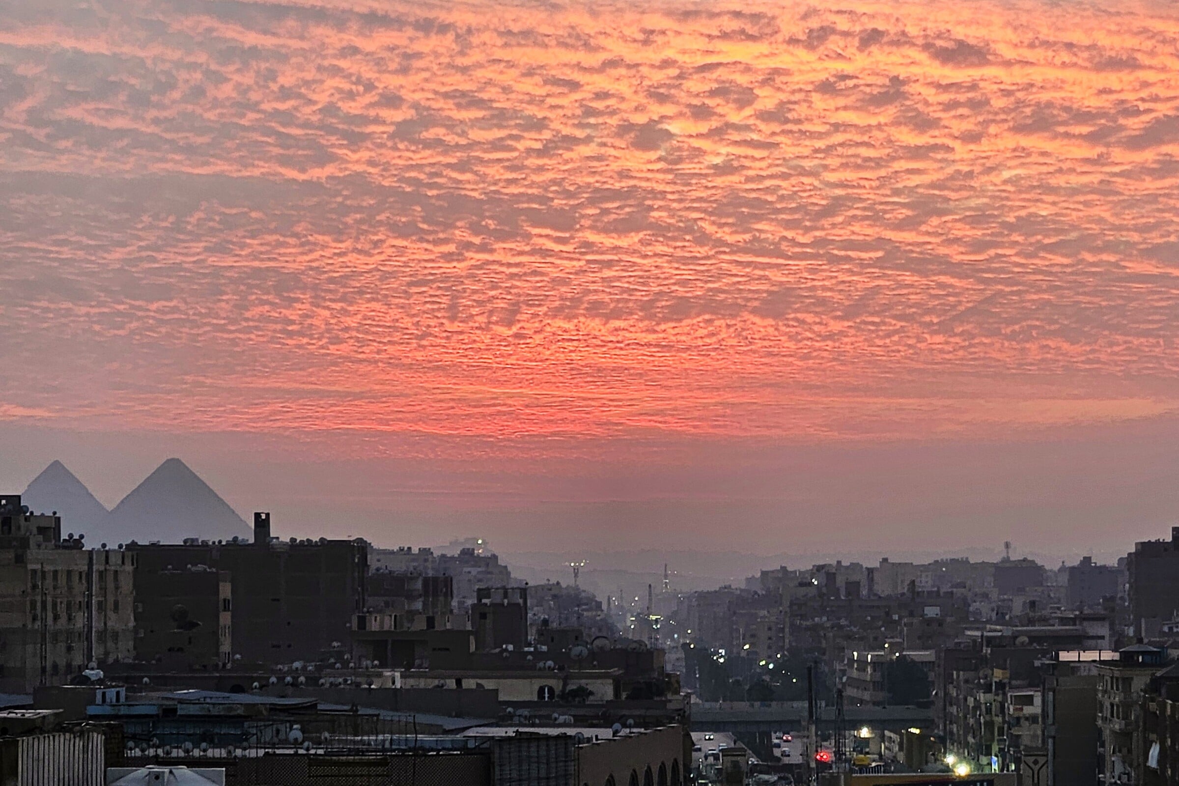 Evening city view of Cairo with the pryamids in the background and a sunset sky.