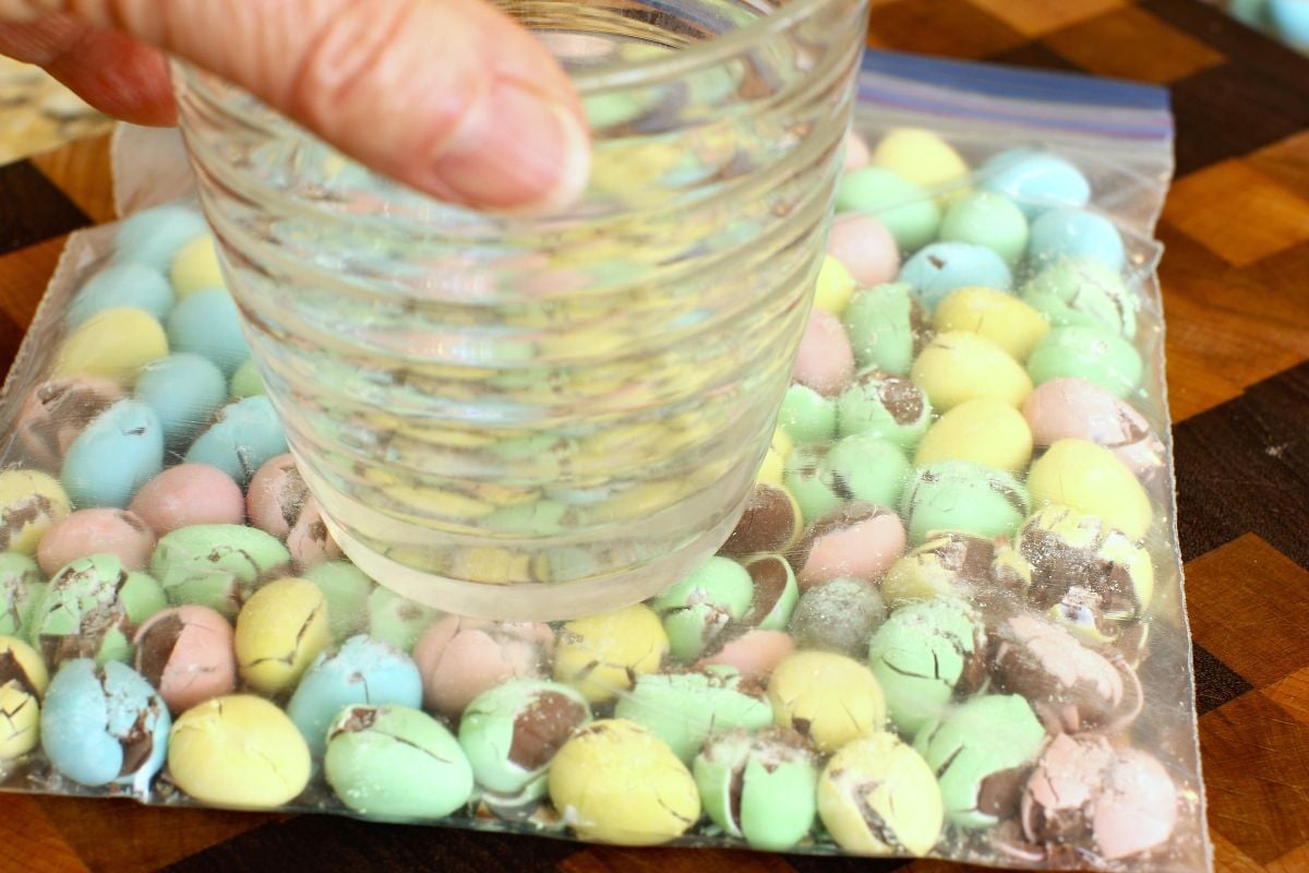 Pressing down on the mini eggs in a plastic bag with a drinking glass to crush them.