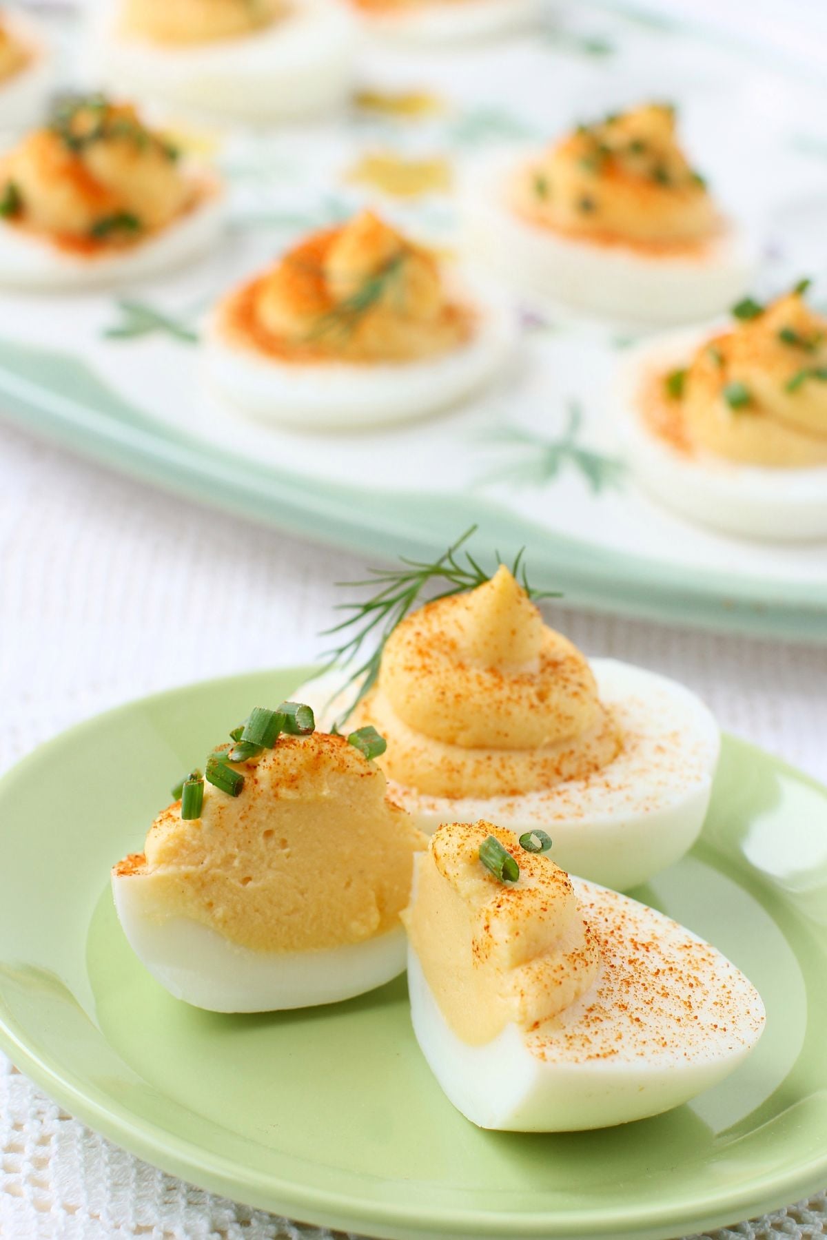 Two devilled eggs on a small green plate, one is cut in half to show the cross section.