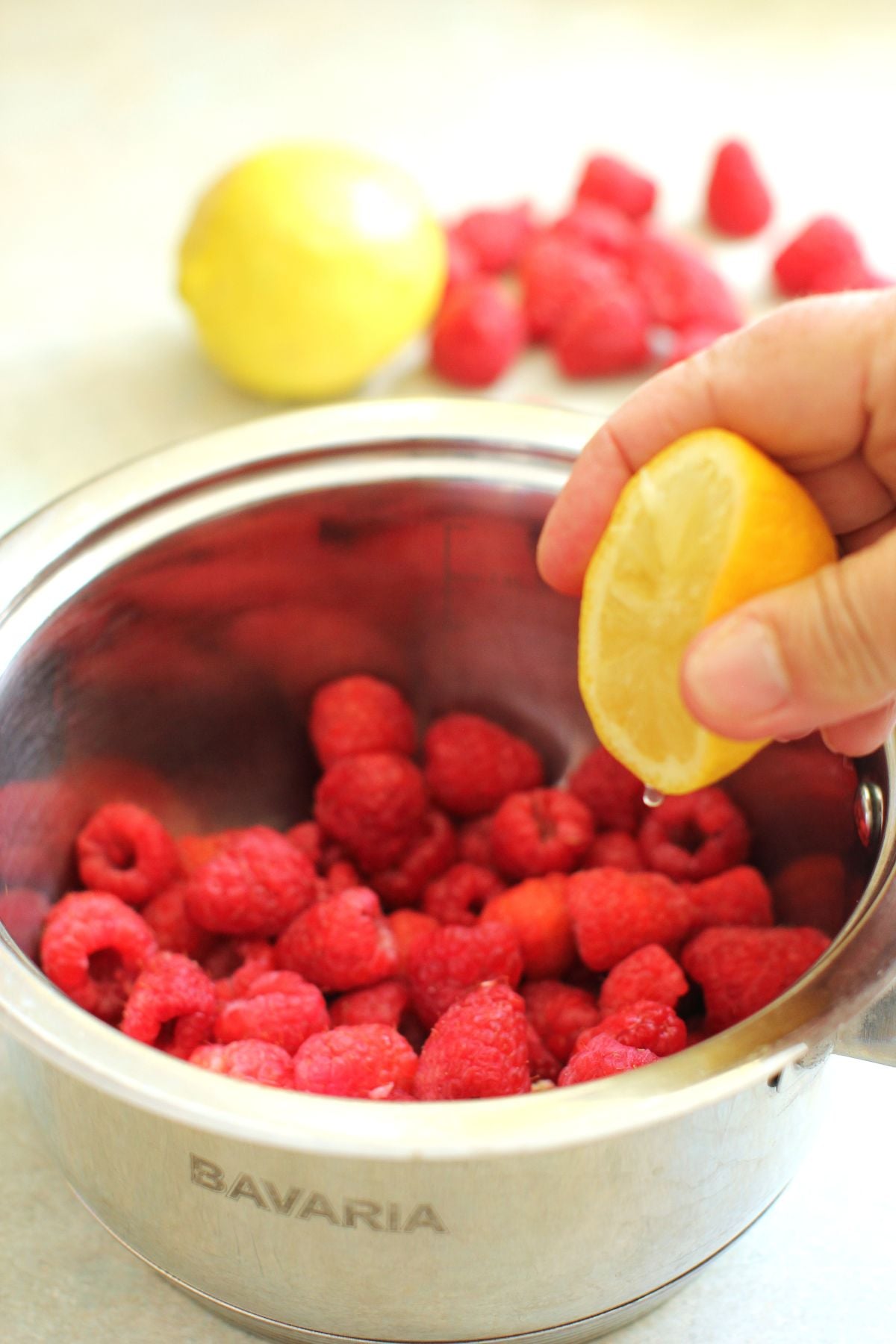 Squeezing a lemon half for juice into the raspberries in a small stainless steel saucepan.