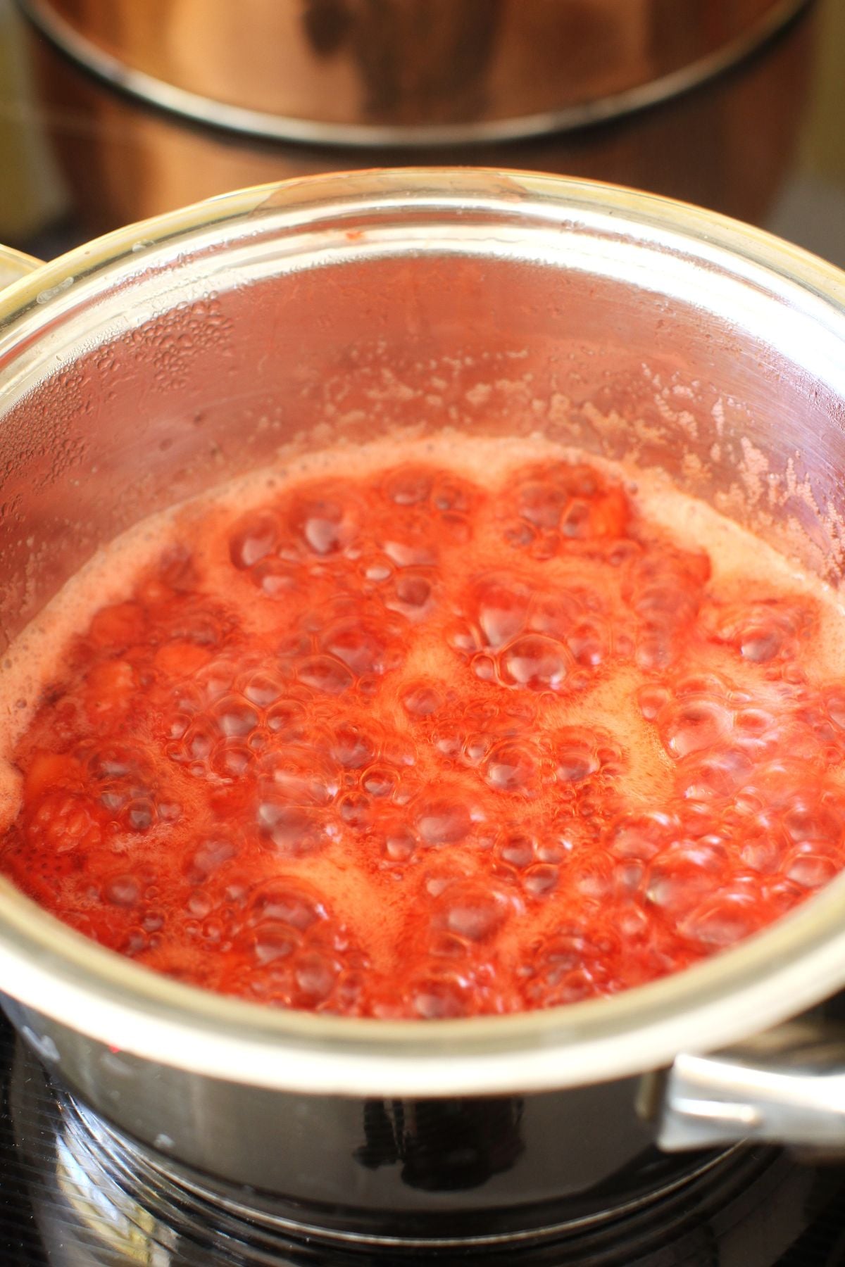 A stainless steel pot on the stove with red raspberry jam bubbling in it.