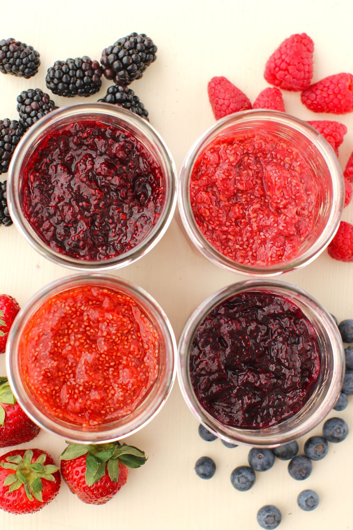 Top-down view of 4 jars of chia jam, with corresponding fruits scattered around each jar.