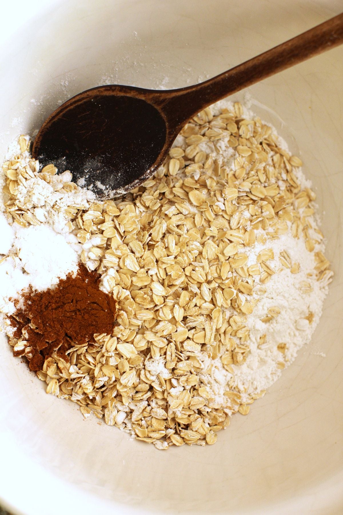 Flour, oats, cinnamon, baking powder, baking soda and salt in a mixing bowl with a wooden spoon