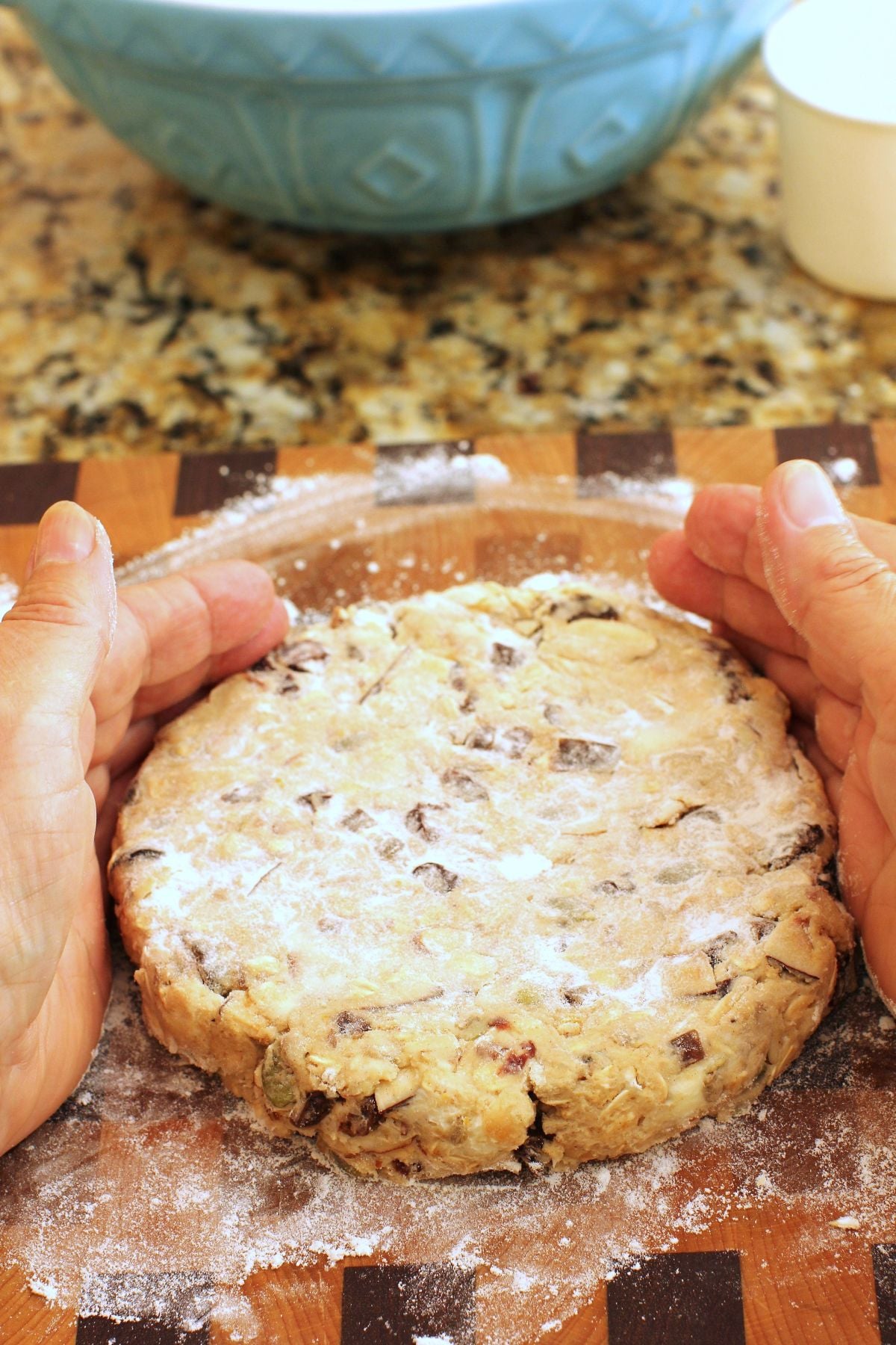 two hands shaping a round disc of dough on a wooden cutting board.