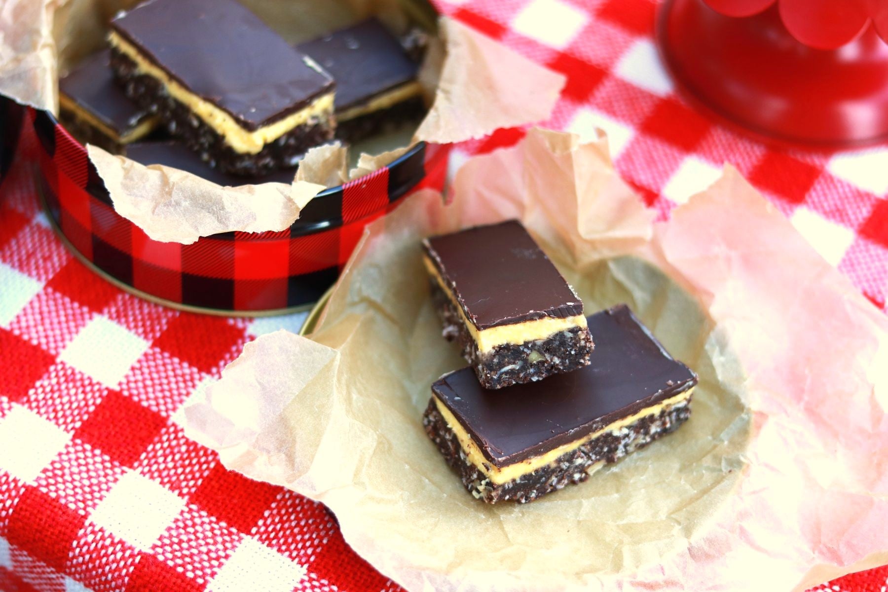 Square thumbnail photo of Nanaimo Bars on crumpled parchment paper on red and white checked cloth.
