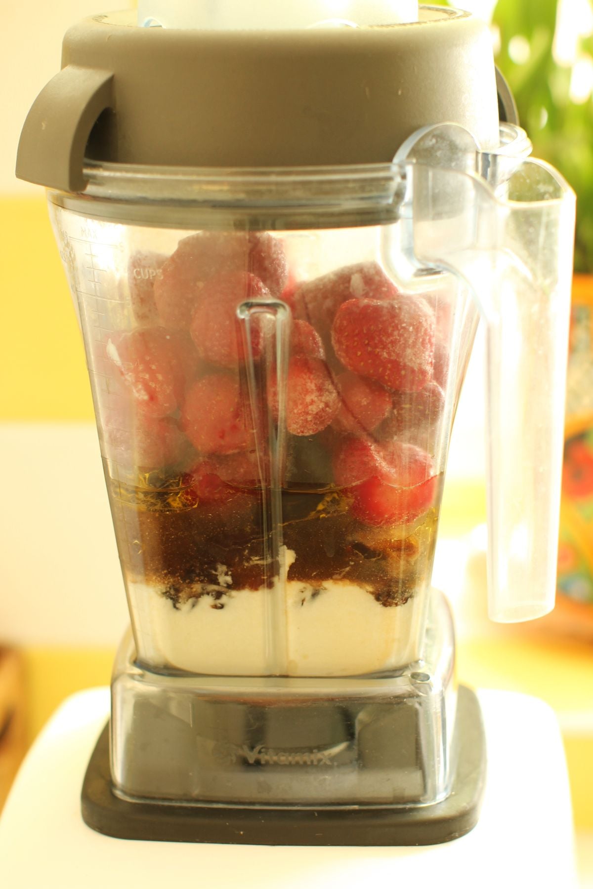 Blender canister with the ingredients for strawberry date smoothies layered in it - yogurt on bottom, thenn dates, then strawberries, vanilla, oil, and water.