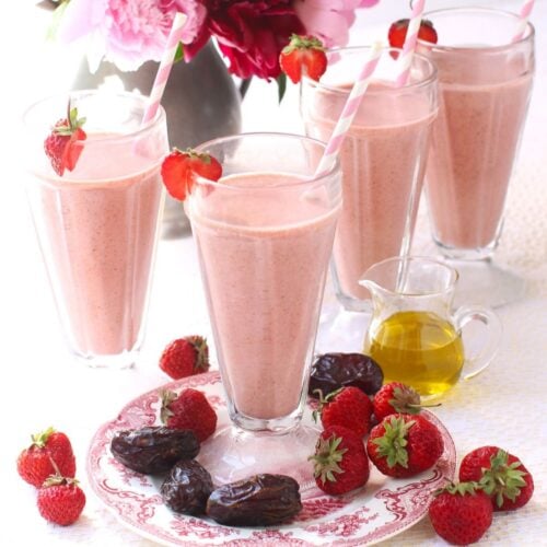 Square thumbnail photo of 3 strawberry date smoothies in tall milkshake glasses, with Medjool dates and strawberries on the table around them.