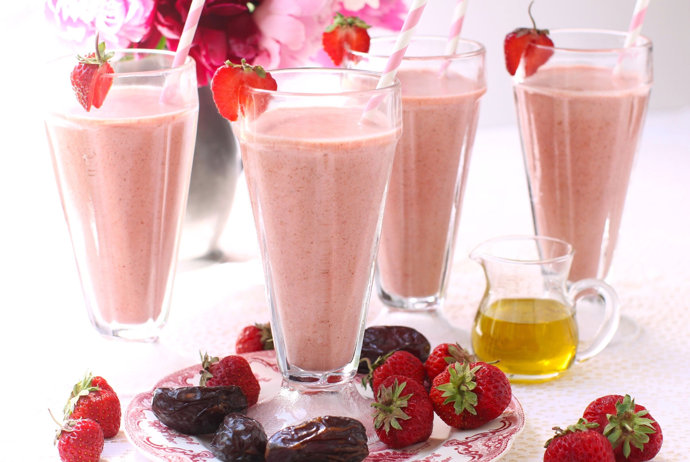 4 tall glasses of smoothie, with dates and strawberries laying in the foreground.